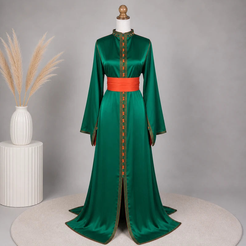 Caftan en drap de soie vert profond avec ceinture orange satinée présenté dans un décor élégant, robe marocaine raffinée idéale pour mariage, cérémonie et soirée orientale chic.
