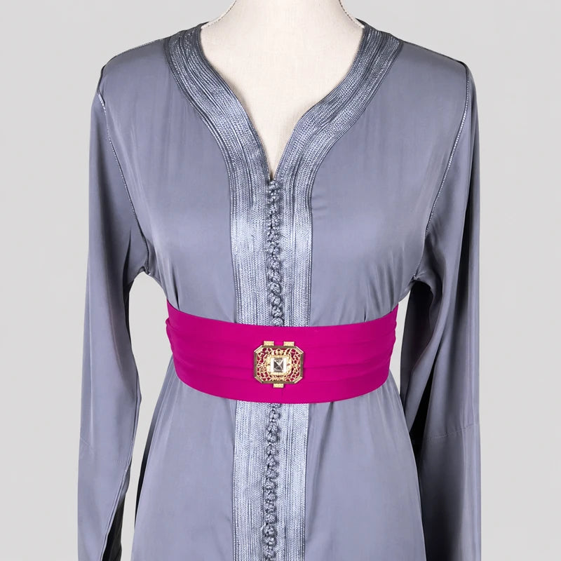 Gros plan sur un caftan marocain simple gris en crêpe mettant en valeur l’encolure traditionnelle, les finitions artisanales et la ceinture fuchsia ornée d’une boucle décorative raffinée.
