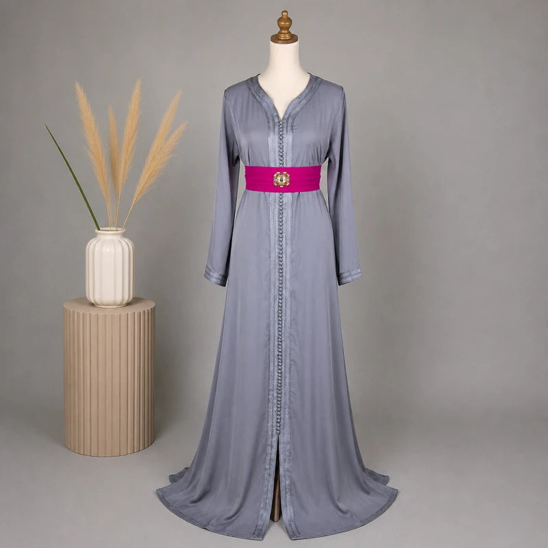 Caftan marocain simple gris en crêpe avec ceinture fuchsia et finitions traditionnelles, présenté sur mannequin dans une mise en scène élégante avec vase décoratif, idéal pour mariage, fête et occasions spéciales.
