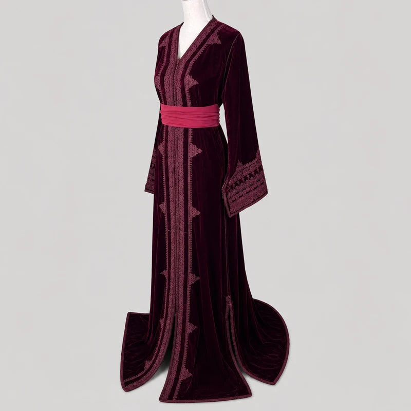 Vue de profil d’un caftan marocain en velours bordeaux brodé avec ceinture rose satinée, manches brodées élégantes et coupe longue raffinée pour mariage et cérémonie.