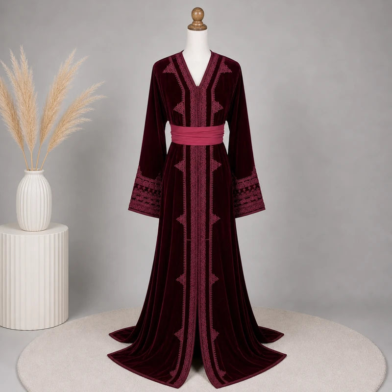 Caftan marocain en velours bordeaux brodé présenté dans un décor élégant avec ceinture rose satinée, robe traditionnelle raffinée idéale pour mariage, fête orientale et cérémonie.