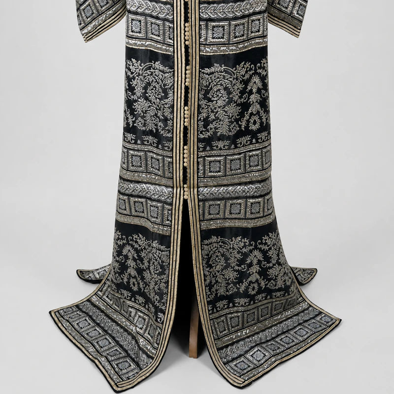 Détail du bas d’un caftan marocain noir vintage avec motifs argentés brocart et finitions dorées élégantes pour femme.