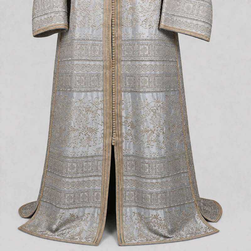 Détail du tissu brocard d’un caftan gris argenté avec motifs dorés raffinés et finitions élégantes, robe orientale traditionnelle haut de gamme pour mariage et cérémonie.