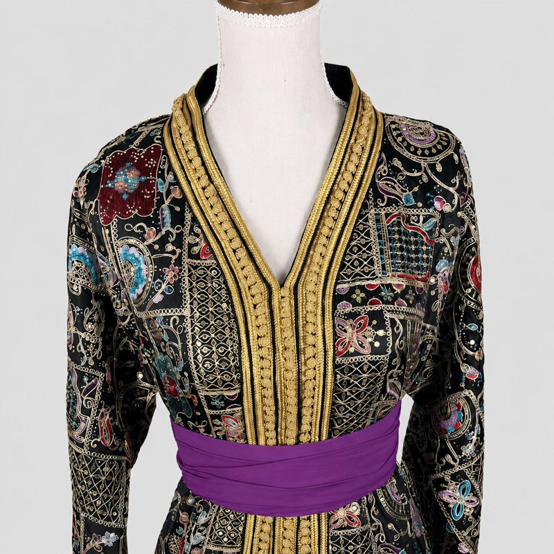 Détail de takchita noire brodée avec ceinture violette et finitions dorées artisanales, caftan marocain élégant pour femme avec motifs orientaux raffinés, col brodé luxe et manches longues, tenue traditionnelle idéale pour mariage marocain et soirée orientale.