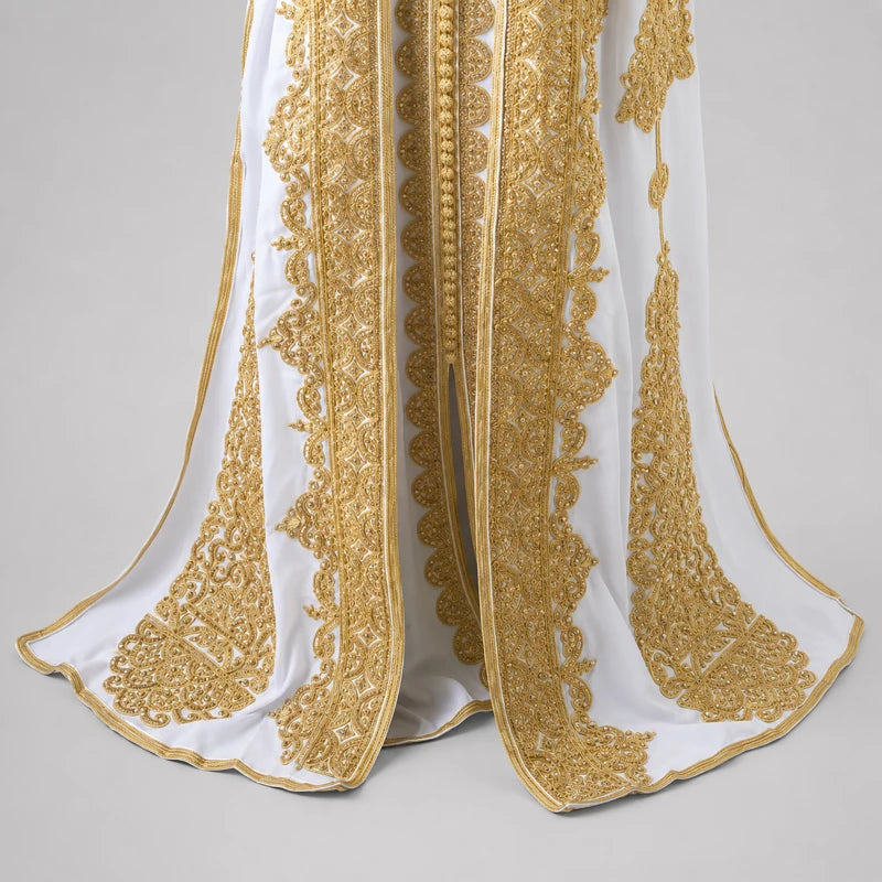 Détail du bas d’une takchita de mariée blanche en crêpe de soie avec broderies dorées artisanales et finitions marocaines élégantes