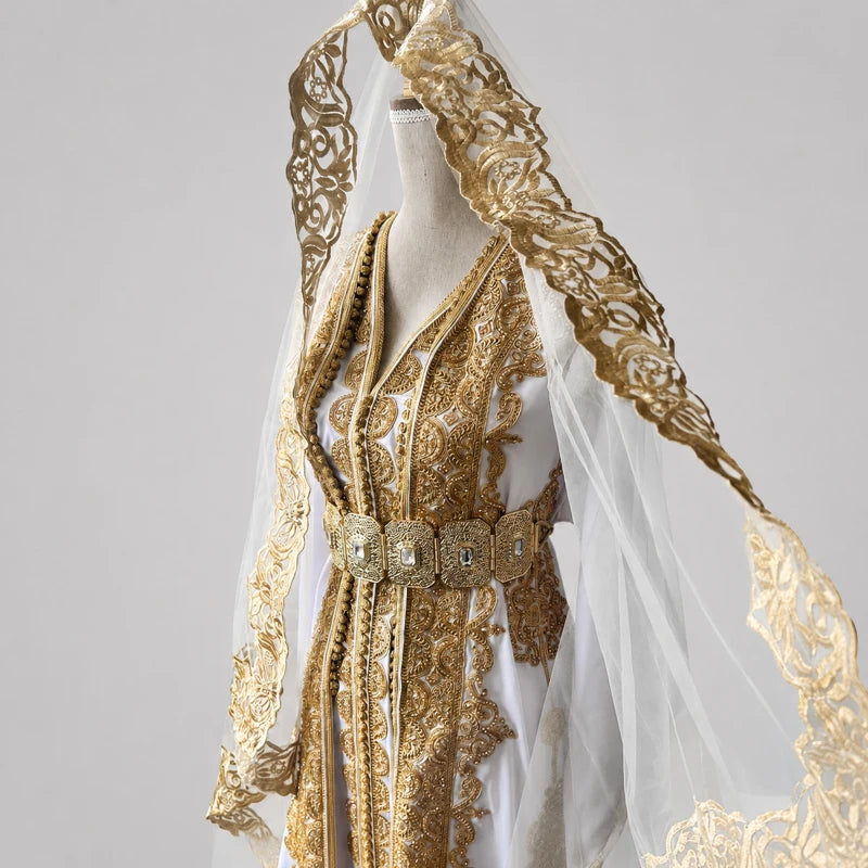Détail haut d’une takchita de mariée blanche en crêpe de soie avec broderies dorées artisanales et voile transparent raffiné, robe marocaine élégante